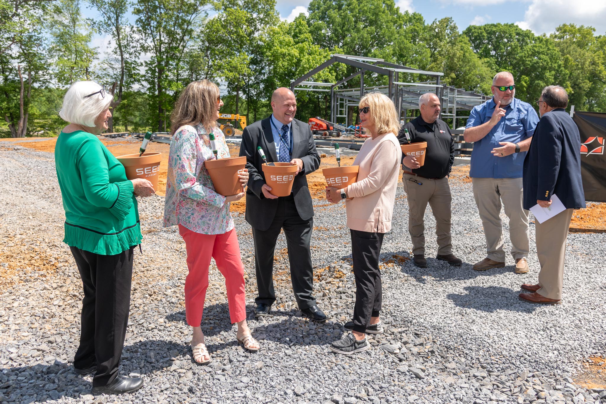 people holding flower pots and talking in front of construction
