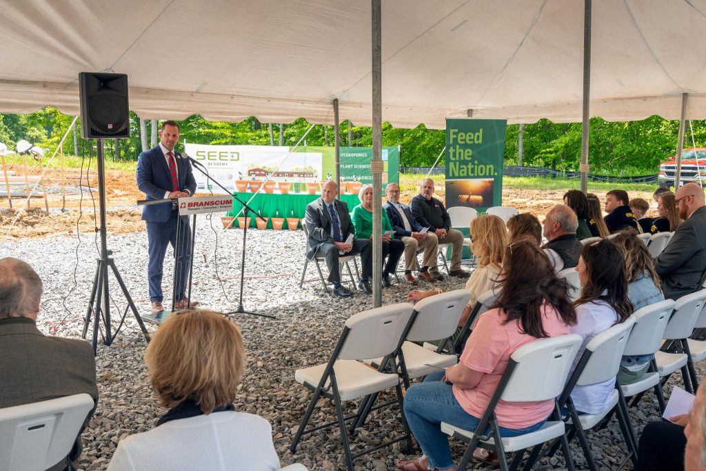 man speaking to group under a tent